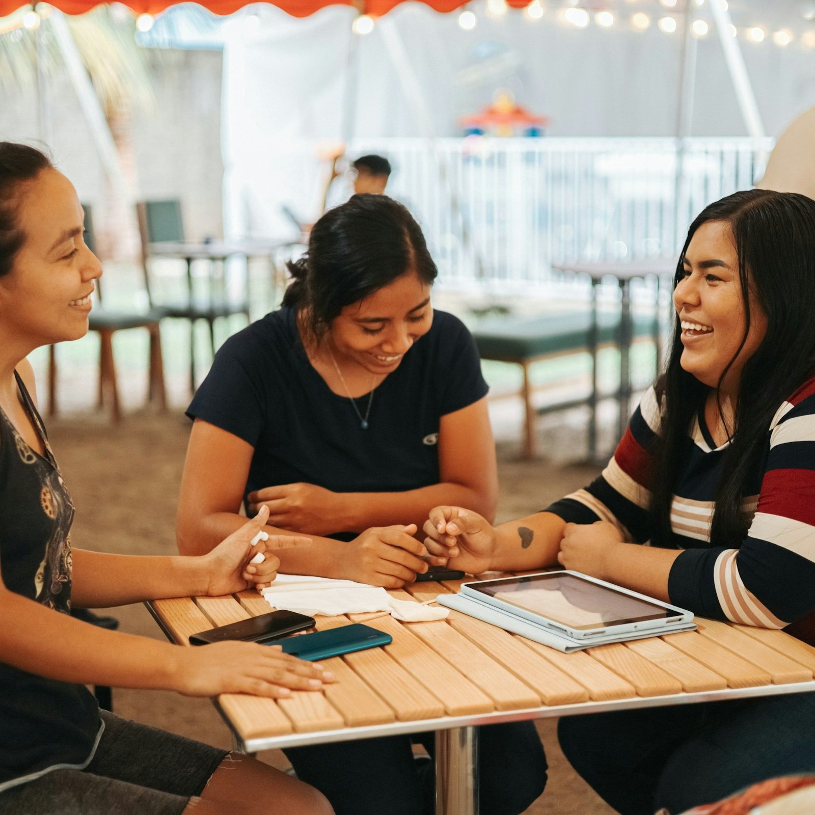 Three friends laughing together at an outdoor table